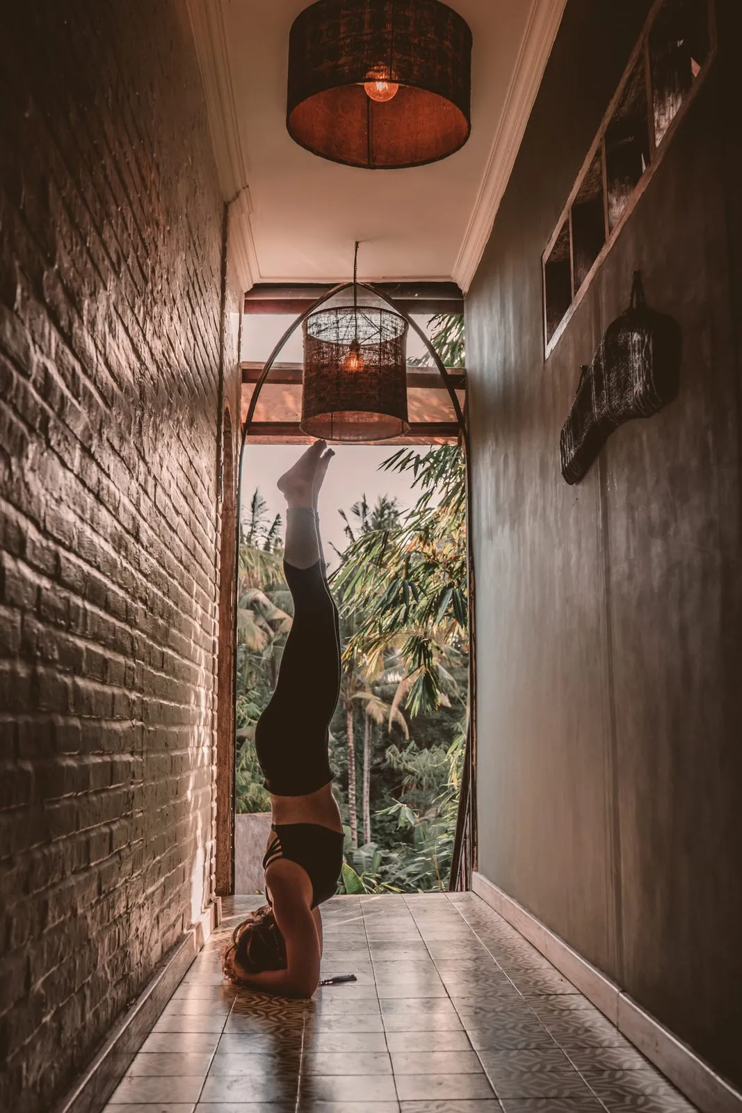 A woman in a headstand in a dark corridor, the jungle bright in the doorway beyond
