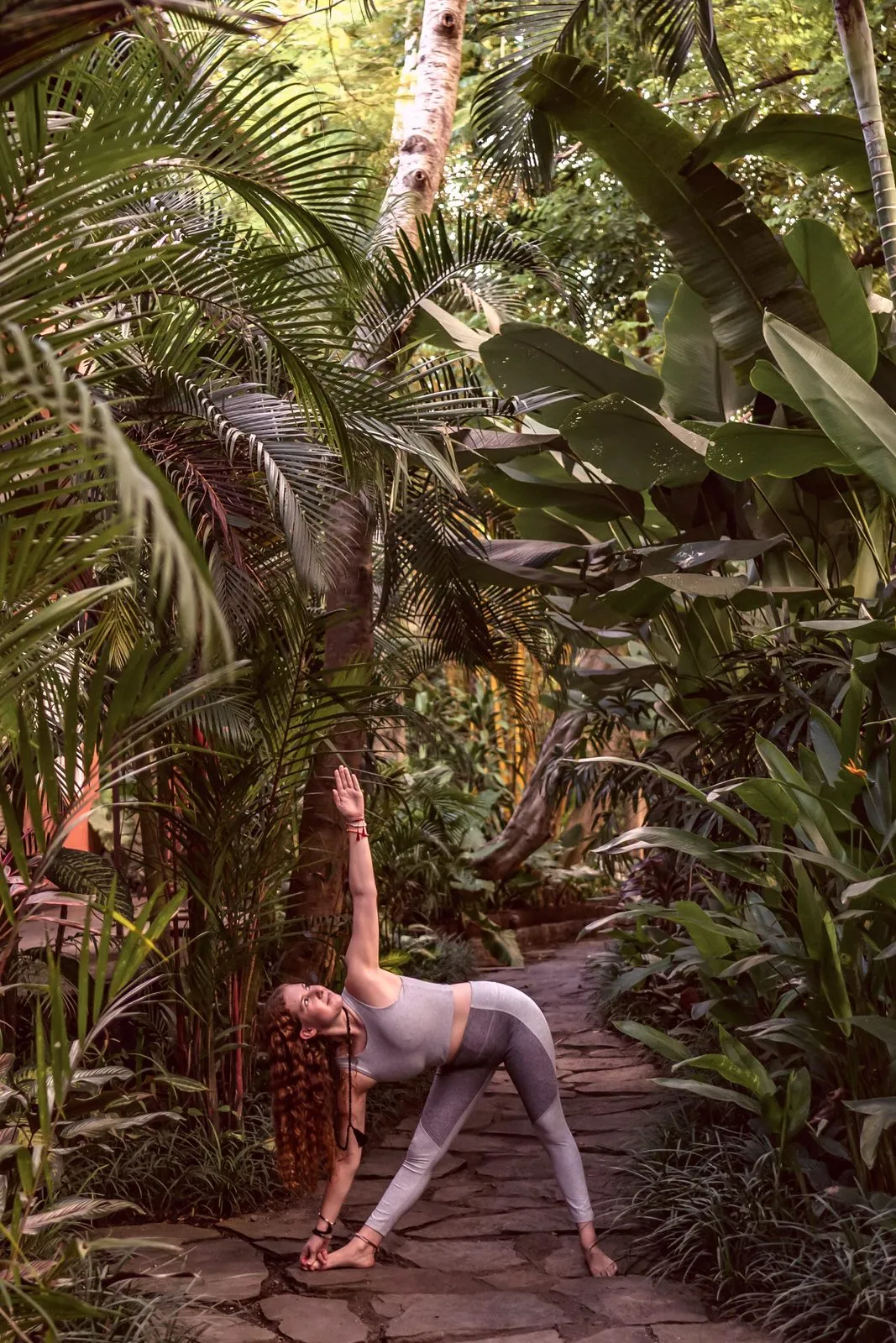 A woman in a standing forward fold on a garden path among banana leaves and palms