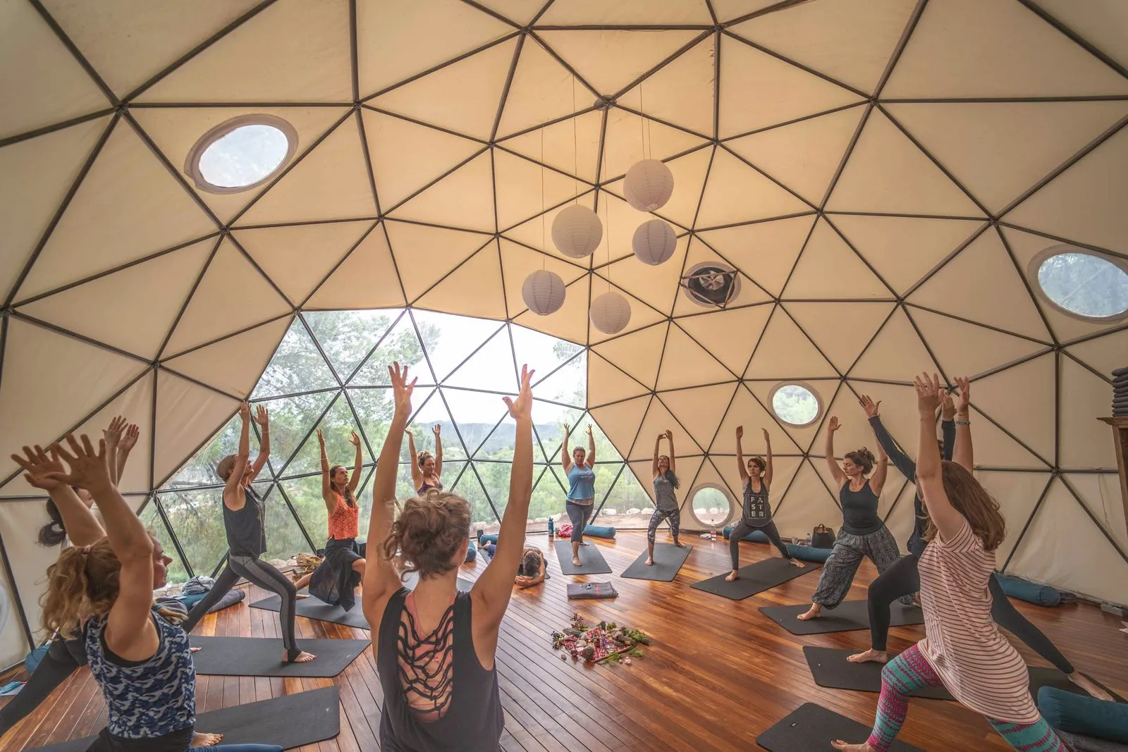 A yoga class reaching up together inside a geodesic dome on a retreat, arched window open to the green
