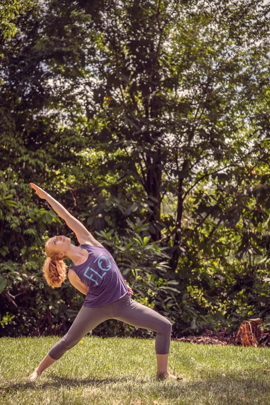 A woman in a purple tank top in extended side angle pose on the grass, arm reaching over her head